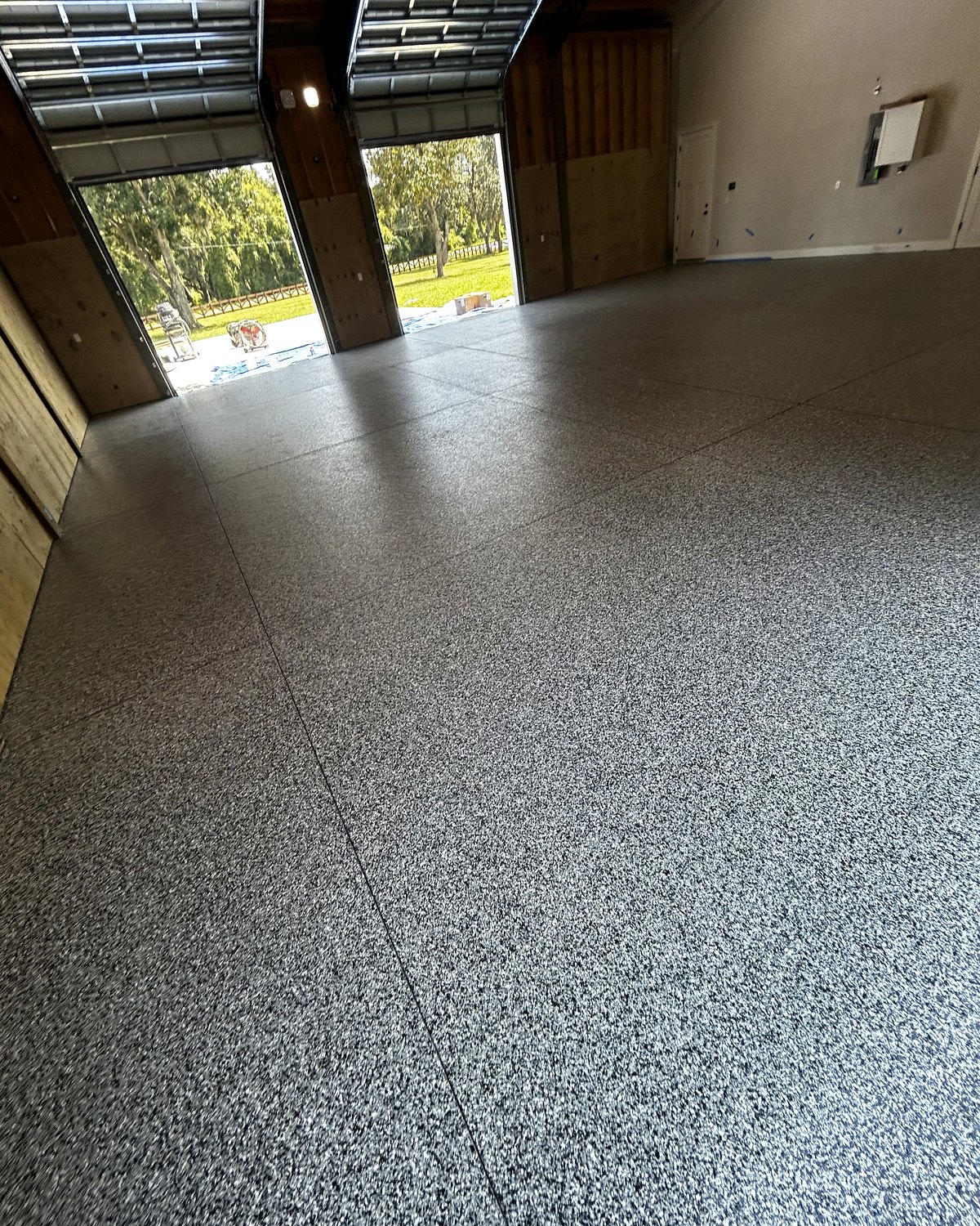 Gray flake epoxy floor across an oversized garage with open overhead doors